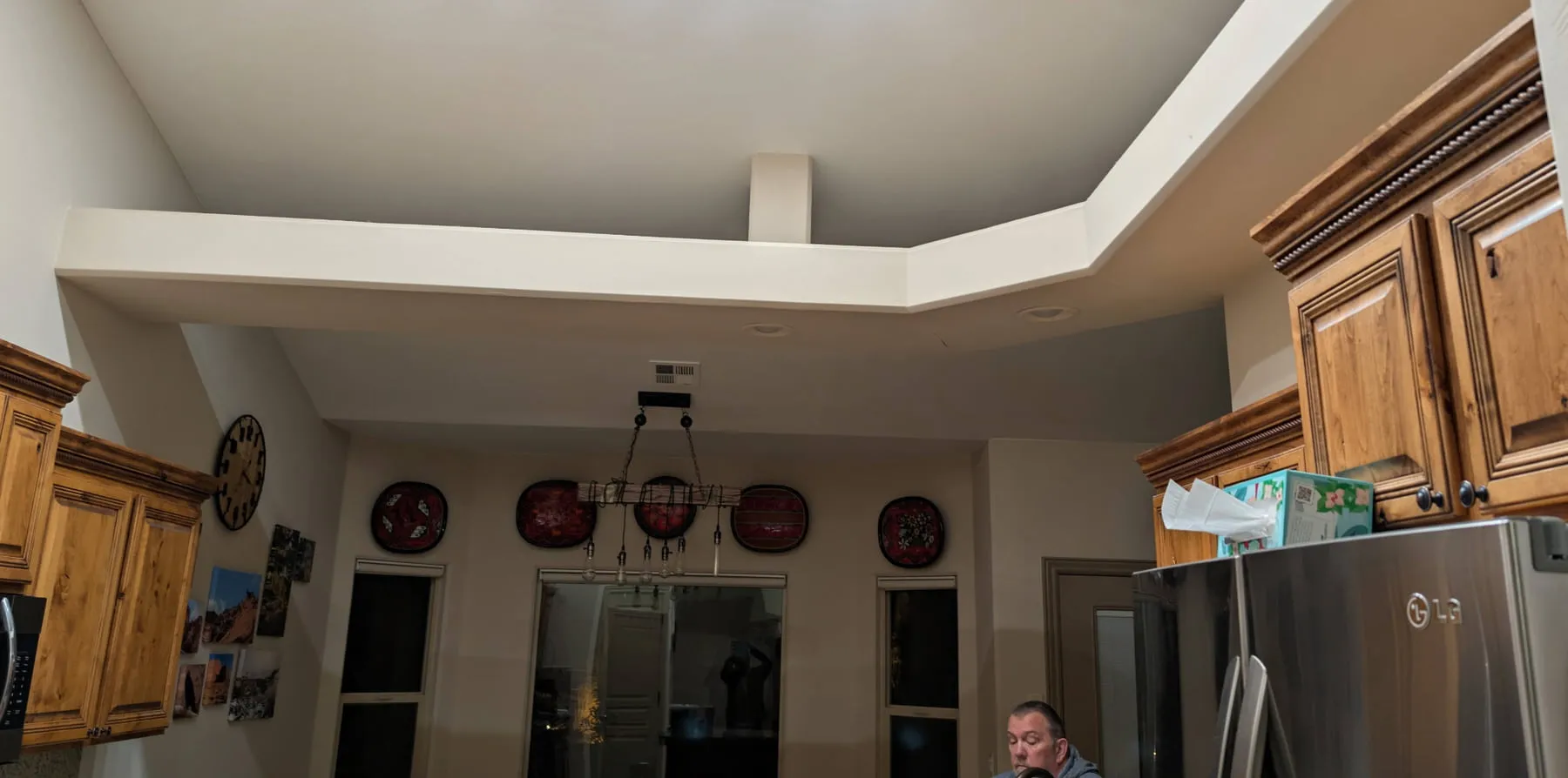 A boxed ceiling soffit with a vent grille and a hanging pendant light fixture bridging two sections of a vaulted kitchen ceiling