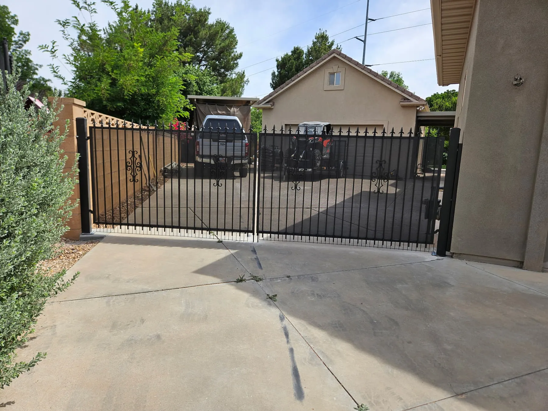 A new matte-black iron double driveway gate with a matching pedestrian gate on black posts, across the same concrete driveway